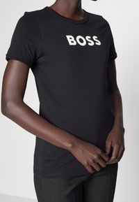 Černé bavlněné tričko s bílým textem "BOSS". Krátké rukávy, kulatý výstřih a těsný střih. Měkká textura, hladký povrch.