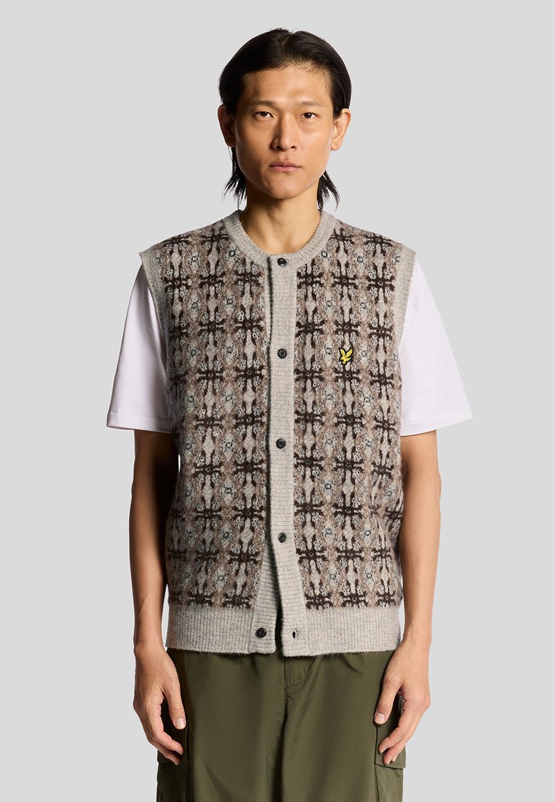 Gilet grigio lavorato a maglia con un motivo testurizzato marrone e beige, chiusura frontale con bottoni e un piccolo logo giallo sul lato sinistro del petto. Indossato sopra una maglietta bianca.