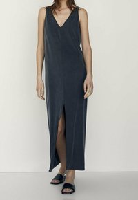 Maxikjole i mørkegrå, med dyb V-udskæring, ærmeløs design og sideslids. Fremstillet af blødt stof med en glat tekstur.