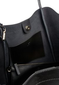 De binnenkant van de zwarte leren tote bag heeft een suede voering, een drukknopsluiting en een ritsvak met een zwarte leren kaartenhouder.