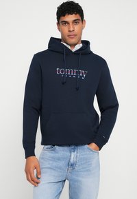 Navy blue hoodie made of cotton blend, featuring a front kangaroo pocket, drawstring hood, and a colorful "tommy jeans" logo on chest.