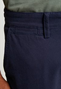 Pantaloni in tessuto blu navy con una finitura tessuta e testurizzata. Presentano una semplice vita e una tasca laterale.