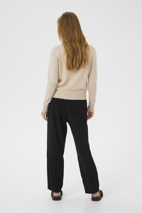 Pull beige en matériau doux, associé à un pantalon noir ample. Design simple, tricot texturé et coupe décontractée. Sandales noires portées.