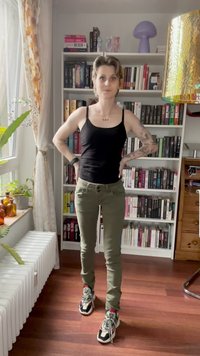 Čierny top na ramienka, olivové nohavice s prednými vreckami a vzorované tenisky. Pozadie obsahuje knižnicu a izbové rastliny.