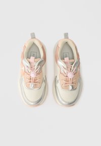 Ζευγάρι ροζ, ασημένια και μπεζ παιδικά αθλητικά παπούτσια με λουλουδάτες λεπτομέρειες και ελαστικά κορδόνια με κλιπ, εμφανισμένα από πάνω σε λευκό φόντο.