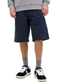 Marinefarbene Cargo-Shorts aus Baumwolle, mit mehreren Seitentaschen, flachem Bund und knielangem Design. Kombiniert mit schwarzen Sneakers und grauen Socken.
