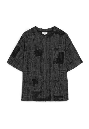 Chemise noire à manches courtes avec un motif imprimé de journaux, présentant diverses textures et motifs sur l'ensemble du tissu. Encolure crew.