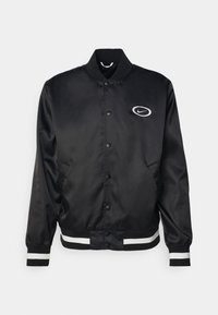 Černá saténová bomber bunda s žebrovaným límcem, patentními knoflíky a bílými pruhovanými detaily na manžetách a lemu. Má na hrudi logo Nike.