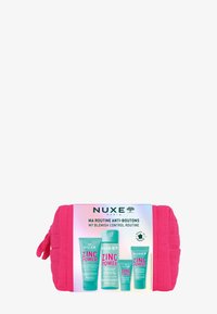 Bolso acolchado rosa que contiene cuatro productos de cuidado de la piel etiquetados como "Zinc Power", con diferentes tamaños y acentos en teal.