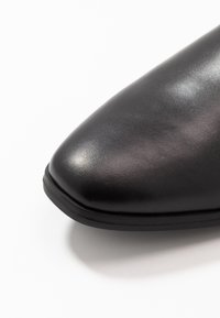 Černá kožená bota se špičatou špičkou, hladkým povrchem a jemným leskem. Nízká, odolná gumová podrážka s elegantním designem.