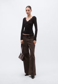 Μαύρο μακρυμάνικο τοπ με δαντελένιο τελείωμα, σε συνδυασμό με καφέ φαρδιά παντελόνια. Το μοντέλο κρατά μια καφέ τσάντα ώμου και φοράει μαύρες μυτερές γόβες.