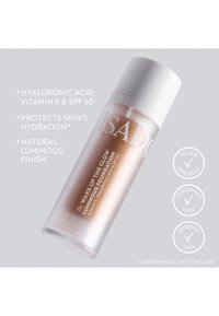 Bouteille en verre translucide avec un bouchon pompe blanc. Contient un fond de teint couleur pêche étiqueté "Wake Up The Glow" avec un SPF 50 et des indications véganes.
