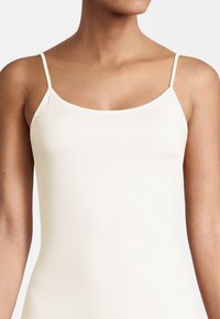 Light beige camisole with thin straps, featuring a smooth, stretchy fabric and a wide neckline. No visible patterns or accents.