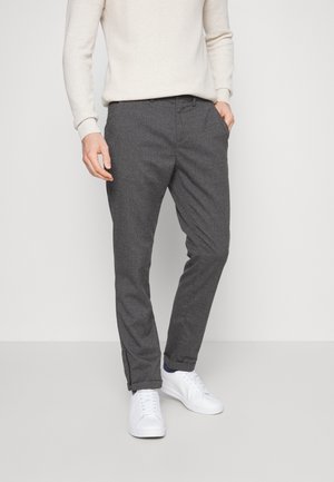 Pantalons gris sur mesure en tissu texturé, avec une coupe slim et des poches latérales. Portés avec un pull léger et des baskets blanches.