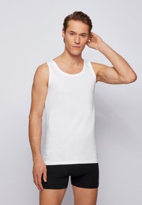 White tank top made of cotton, featuring a scoop neckline and wide shoulder straps, paired with black boxer shorts. Smooth texture.