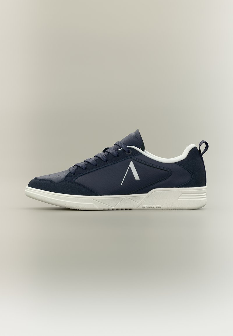 Ναυτικό μπλε αθλητικό παπούτσι χαμηλού τύπου με λευκή σόλα, κορδόνια και γωνιακό λογότυπο "A" στο πλάι, εμφανιζόμενο σε προφίλ σε ουδέτερο φόντο.