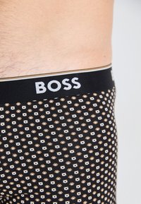 Schwarze Boxer-Briefs mit einem gemusterten Design, das kleine weiße und goldene Diamanten zeigt. Logo "BOSS" auf dem elastischen Bund in Weiß.