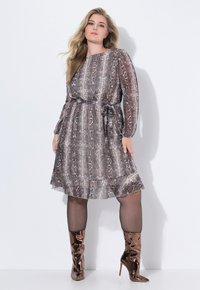 Braun-schlangenbedrucktes Kleid mit langen Ärmeln und einem Taillengurt. Getragen mit glänzenden braunen, knielangen Stöckelschuhen. Glattes, fließendes Material, mittellang.
