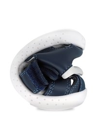 Zapato de piel navy con suela blanca perforada. Correa de velcro y forma curvada para un ajuste seguro. Textura suave con detalles de costura en contraste.