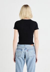 Svart kortärmad topp med figurnära passform, kombinerad med ljusblå högmidjade jeans med bakfickor och logotyp på midjebandet.