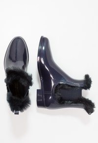 Purple glossy ankle boots with a faux fur trim, elastic side panels, and a low block heel, featuring a shiny, smooth texture.