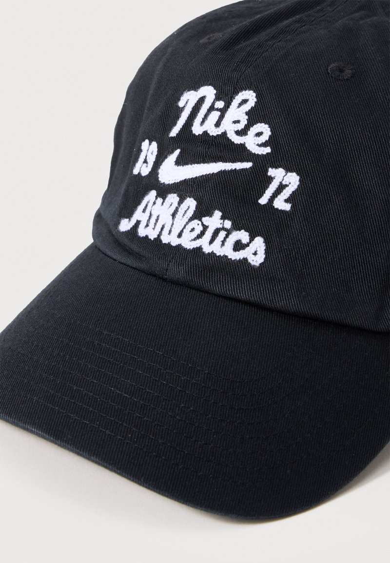 Gorra de béisbol negra de Nike con texto blanco bordado "Nike Athletics" y los números "19" y "72" a ambos lados del logo Nike swoosh.