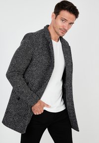 Fekete-fehér houndstooth mintás gyapjúkeverék kabát, sálgallérral, testhez álló szabással és oldalsó zsebekkel. Sima textúra.