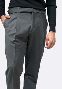 Pantaloni grigi su misura realizzati in un tessuto liscio. Presentano una cintura con fibbia in metallo, tasche laterali e una finitura lucida.