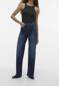 Mörkblå raka jeans av denim med hög midja, fem fickor och en ren finish. Kombinerat med en svart ärmlös topp.