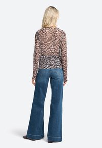 Sheer long-sleeve top in a leopard print design with a gradual color transition, paired with wide-leg blue denim jeans featuring a stitched hem.