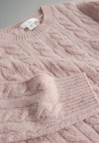 Jasnoróżowy sweter z dzianiny z motywem warkoczowym i prążkowanym dekoltem okrągłym, z teksturowanymi akcentami na całej powierzchni materiału.