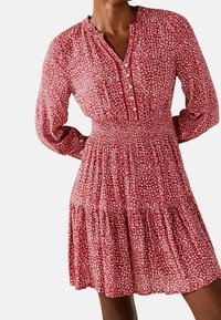 Rotes Blumenkleid mit langen Ärmeln, einem durchknöpfbaren Ausschnitt und einem gerafften Bund. Verfügt über einen gestuften Rock und einen leichten, strukturierten Stoff.