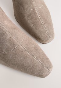 Suede ankle boots in beige with a pointed toe. Features contrast stitching and smooth surface texture. No visible hardware or embellishments.