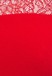 Haut en tissu rouge avec une partie inférieure texturée et une partie supérieure en dentelle ornée de motifs floraux complexes. Matériau fin et doux dans l'ensemble.