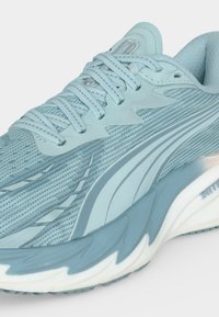 Chaussure de sport bleu clair en mesh avec lacets assortis, empeigne texturée et semelle épaisse blanche et bleue conçue pour la course ou une utilisation décontractée.