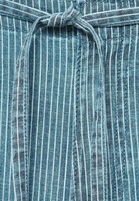 Tissu bleu clair à rayures avec des fines lignes blanches, doté d'une fermeture à nouer à la taille et d'un tissage texturé.