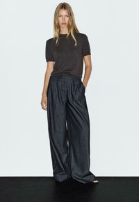 Donkergrijze t-shirt met korte mouwen, gecombineerd met losse, wijde denim broek, met een gladde textuur en subtiele glans.