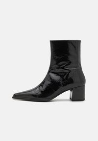 Botine negre din piele lacuită, cu vârf ascuțit, partea superioară structurată și toc gros. Prezintă o textură netedă și strălucitoare.