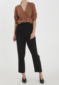 Cardigan marrone a coste con scollo a V profondo e tre bottoni, abbinato a pantaloni neri a vita alta con cintura in vita e gamba affusolata.