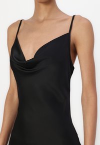 Svart satengdress med cowl-hals, tynne stropper og en stram, figursydd silhuett. Glatt tekstur og minimalt design.
