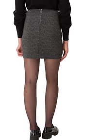 Jupe mini grise à motifs avec une fermeture éclair au dos, associée à des collants noirs transparents et des chaussures noires en vernis.