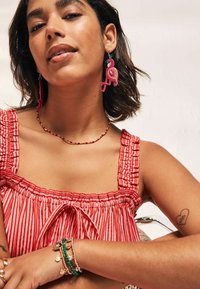 Orecchini a forma di fenicottero rosa, top a righe rosse e bianche, collana di perline, vari bracciali in metallo e di perline, pelle liscia, acconciatura casual.