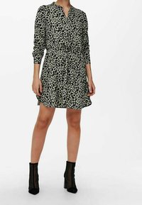 Särskilt klänning med leopardskprint i olivgrön med svarta fläckar, långa ärmar, knapplist framtill och insnävd midja; matchad med svarta ankelboots.