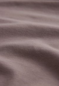 Zachte, lichte mauve stof met subtiele textuur en zachte kreukels, die een glad oppervlak en variaties in tint laat zien.