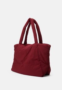Red quilted tote bag with two padded handles, rectangular shape, and crinkled texture, featuring seams for structure.