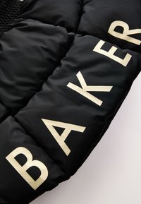 Tela acolchada negra con grandes letras blancas formando la palabra "BAKER" en diagonal a lo largo de la superficie.