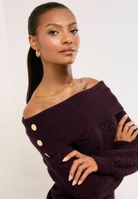 Olkapäät paljastava, burgundinpunainen neulepaita, jossa on letinmuotoinen kuvio ja kullanväriset napit olkapäällä. Sileä pinta ja rento istuvuus.