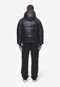 Svart puffjacka med glansig yta, huva och horisontell sömnad; kombinerad med svarta cargobyxor och vita sneakers.