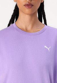 Tricou din bumbac purpuriu cu guler tip crew, prezentând un logo alb Puma pe partea stângă a pieptului. Textură netedă, croială lejeră.