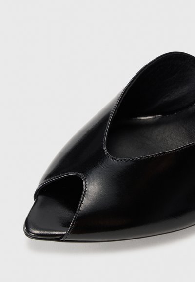 Chaussure ouverte en cuir noir au design épuré, dotée d'une découpe courbée et d'une texture lisse et brillante, avec un petit talon carré.